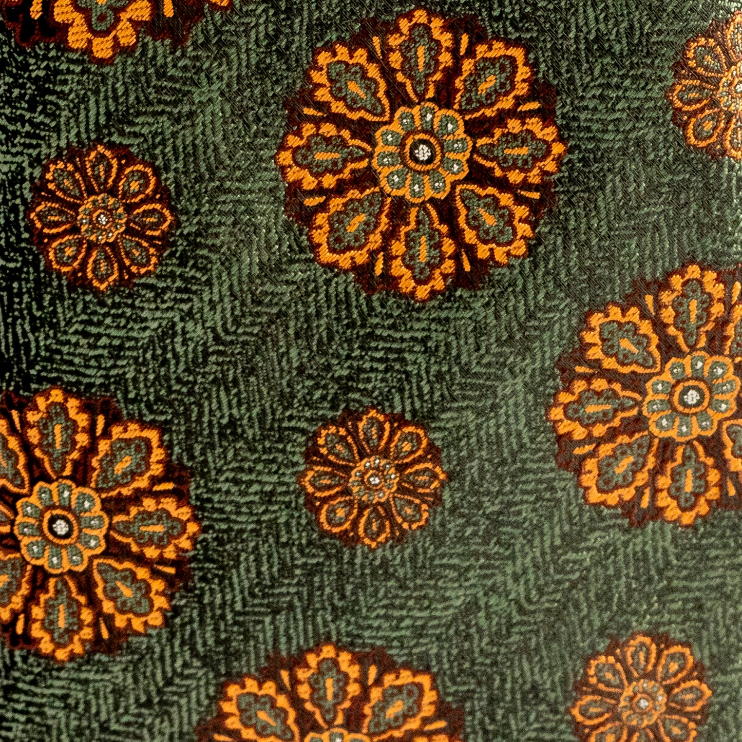 Close-up of a textured fabric with orange floral patterns on a green background