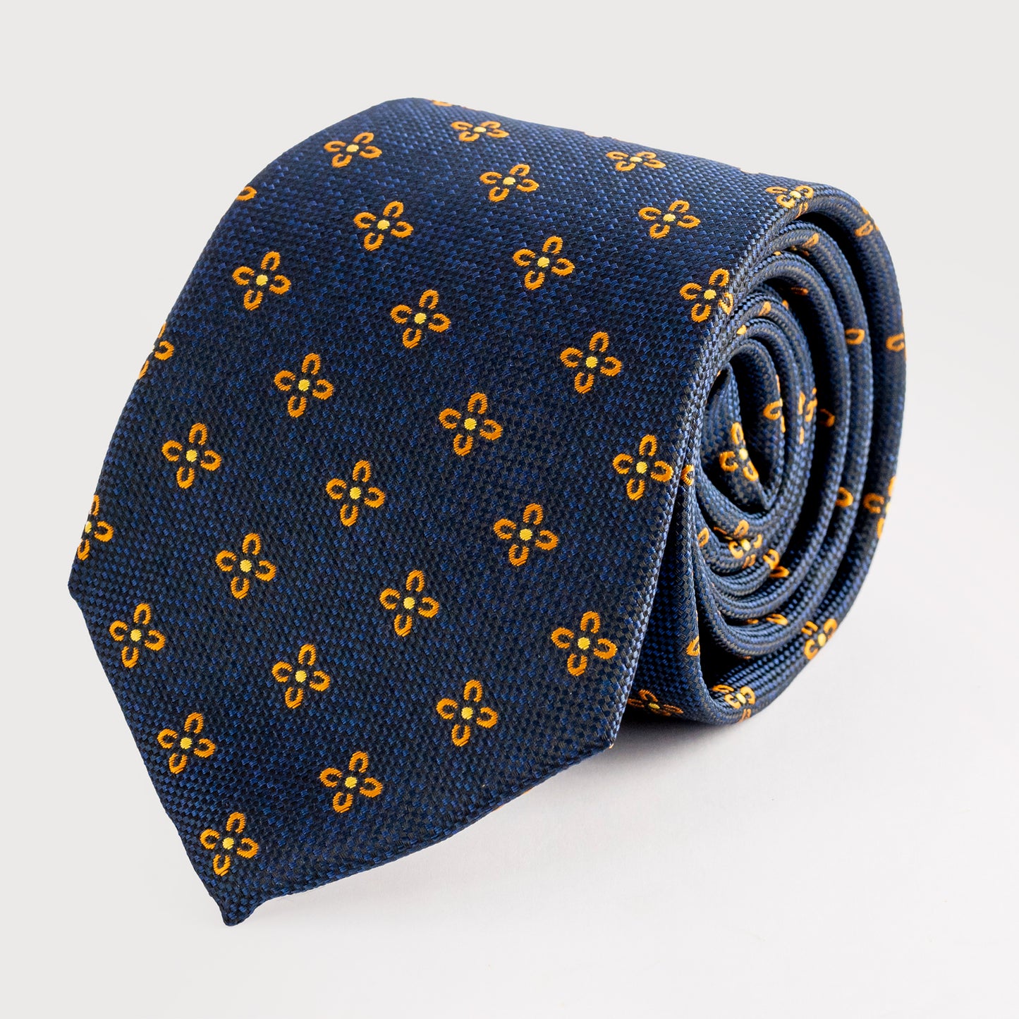 Rolled-up blue tie with yellow floral pattern on a light gray background