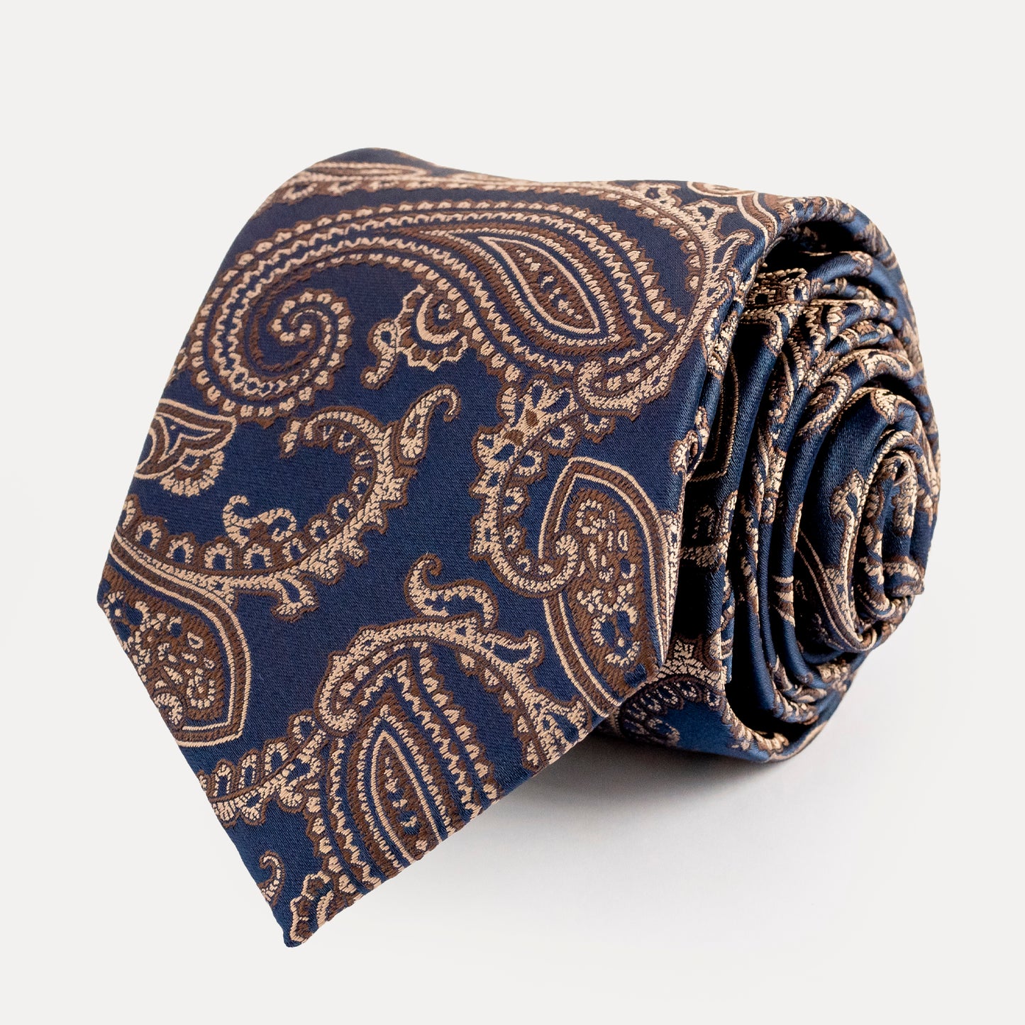 Roll of blue and gold paisley patterned tie on a white background